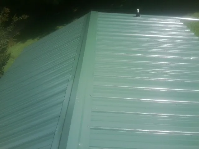 New green metal panels meeting at the ridge of a roof — Flat Roof Repair work by our crew in Uniontown