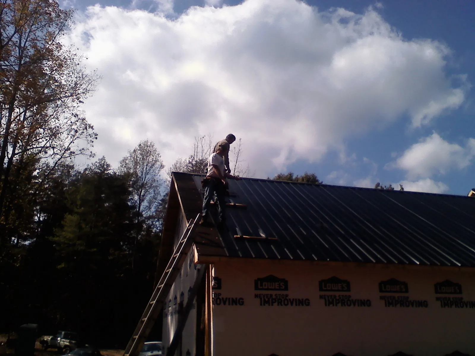 Roofer fastening dark metal panels high against a cloudy sky, from a Roof Inspection job in Uniontown
