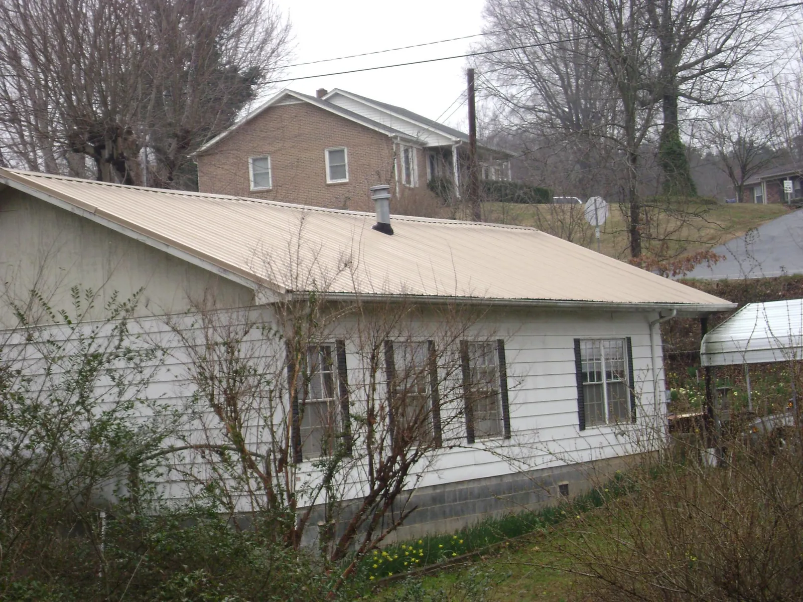 Tan metal roof on a white sided house set into a hillside — Commercial Roofing by Roofing Brothers in Uniontown